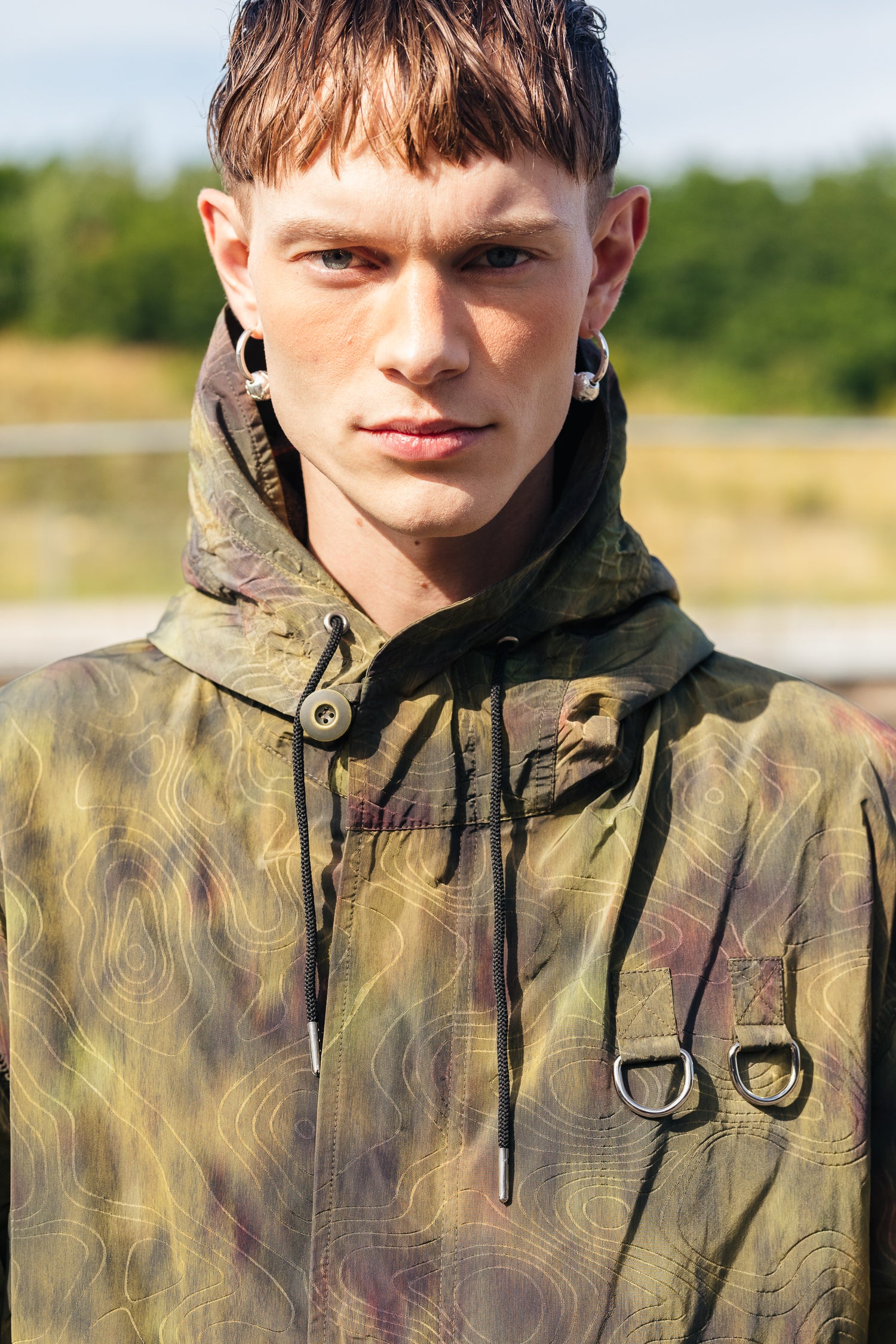 Mallilla on RAKAS Rolf Ekroth x Kalevala -korut korvissaan. Hän katsoo suoraan kameraan ja hänellä on vihreäsävyinen takki.